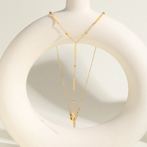 Gros plan sur le collier Y en acier inoxydable doré sur un socle blanc minimaliste