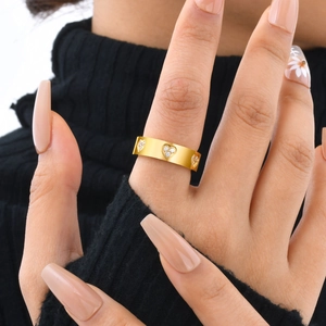 Close-up of a wide gold-plated ring featuring three hollow heart shapes set with cubic zirconia