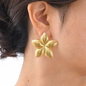 Détail macro d'une boucle d'oreille fleur dorée avec pétales texturés sur le modèle