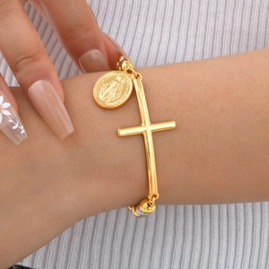 Dettaglio di un bracciale a sfere dorate con croce e medaglia religiosa sul polso