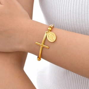 Dettaglio del bracciale dorato a sfere con croce e medaglia religiosa indossato al polso
