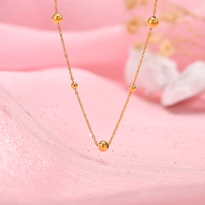 Détail d'un collier en acier inoxydable doré à cinq perles polies sur de la soie rose