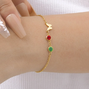 Détail du bracelet papillon doré avec pierres de zircone rouge et verte porté au poignet