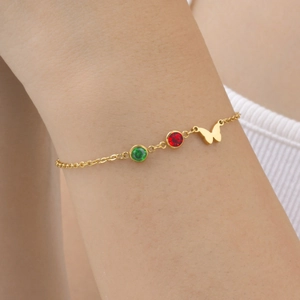 Bracelet chaîne papillon doré avec zircons rouges et verts porté au poignet délicat
