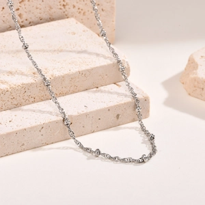 Detail shot of a minimalist silver beaded chain necklace draped on a textured stone base