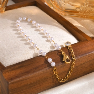 Elegant gold chain bracelet with white pearls and a sparkling zircon charm in a wooden tray