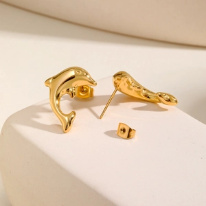 Macro shot of polished golden dolphin stud earrings on a minimalist stone pedestal