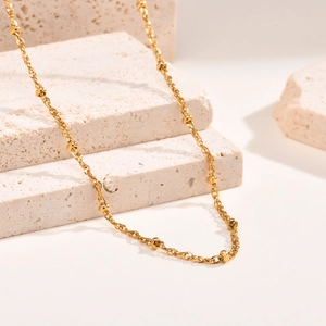 Polished gold stainless steel bead chain necklace displayed on minimalist stone blocks