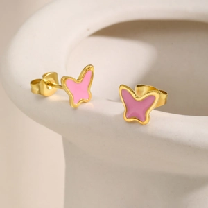 Dettaglio degli orecchini a farfalla dorati con smalto rosa su bordo ceramica