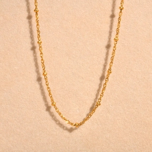 Detail of golden stainless steel ball chain necklace on a warm sandy background