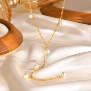 Dettaglio della collana in acciaio dorato con perle bianche su sfondo di raso beige