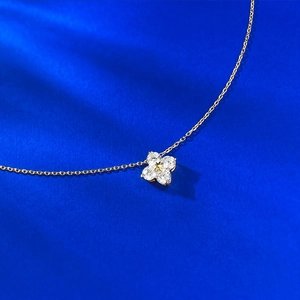 Elegant gold clover necklace with sparkling white crystals on deep blue textured background
