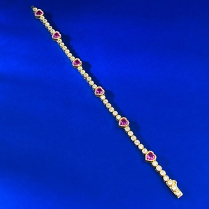 Detail view of gold-plated tennis bracelet featuring pink heart gems and white zircons