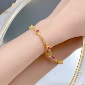 Detail of a gold-plated bracelet with red heart gems and white diamonds on a wrist