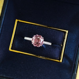 Macro detail of round pink gemstone ring with pavé diamond band in premium gift box
