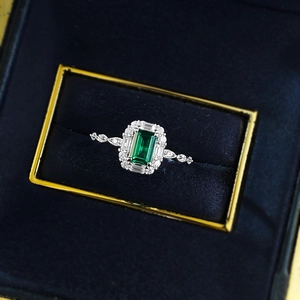 Detailed close-up of emerald-cut green gemstone ring with diamonds in blue velvet box
