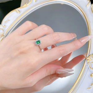 Macro detail of emerald-cut green gemstone ring with silver band and pave accents on hand