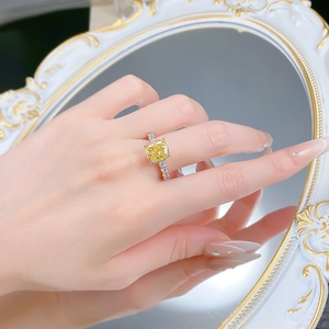 Close-up of a silver cushion-cut yellow diamond ring shown on a finger with mirror reflection