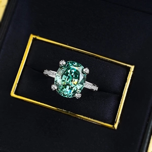 Macro d'une bague avec pierre ovale verte et accents de diamants dans un écrin
