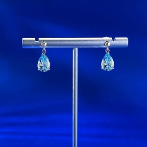 Macro detail of pear-cut light blue gemstone earrings on a silver jewelry stand