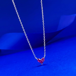 Dettaglio di una collana in argento con ciondolo a cuore rosso su sfondo blu intenso