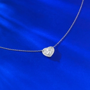 Close-up of heart-cut clear gemstone necklace with halo setting on blue silk