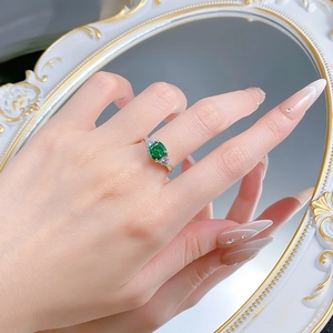 Detailed view of an emerald green square cut gemstone ring with side diamond accents