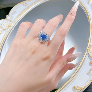 Détail d'une bague avec pierre bleue en forme de cœur et halo de diamants au doigt