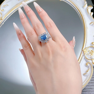 Gros plan d'une bague saphir en forme de cœur avec halo de diamants portée