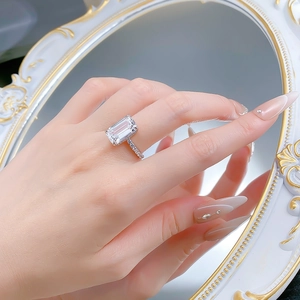 Macro shot of 9x14mm emerald cut gemstone ring with pave diamonds on model finger