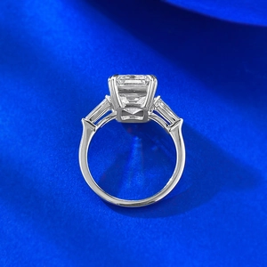 Macro detail of emerald cut three-stone ring with silver band on blue silk background