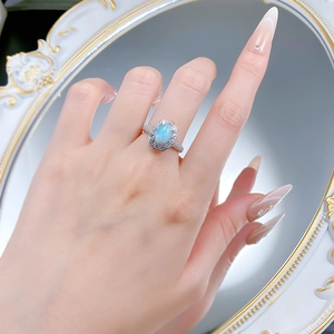 Détail d'une bague ovale en Larimar bleu avec halo de zircons portée au doigt