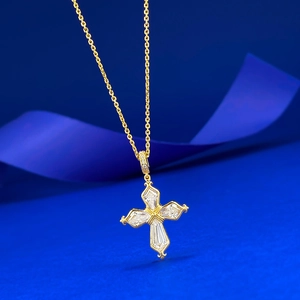 Detail of gold cross necklace with baguette-cut crystals on textured blue background