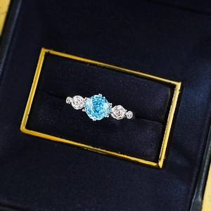Floral silver ring with light blue gemstone and rose details in a velvet jewelry box