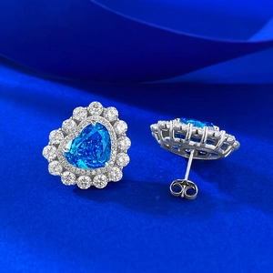 Makrodetail von herzförmigen blauen Topas-Ohrringen mit Halo-Diamanten auf Seidenhintergrund