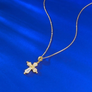 Macro shot of gold iris cross pendant with clear crystals on blue silk background