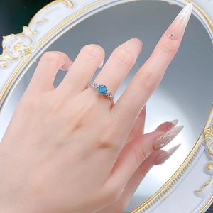 Detail of silver rose wreath ring with blue round cut gemstone worn on finger