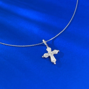 Macro detail of S925 silver iris cross pendant with inset crystals on blue silk background