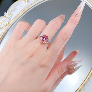 Gros plan d'une bague élégante avec pierre rose et halo de diamants portée au doigt
