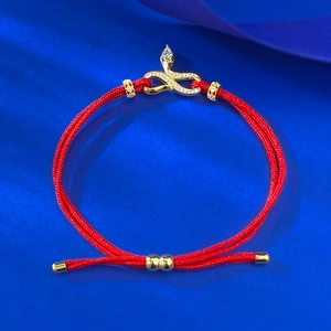 Macro shot of gold plated snake charm with white zircons on red braided bracelet