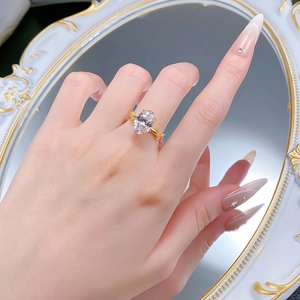 Détail d'une bague avec cristal ovale serti de griffes dorées portée au doigt