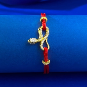 Detailed macro view of S925 silver gold-plated snake charm on red woven rope bracelet