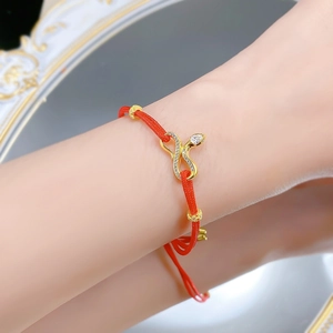 Detail of red braided string bracelet with gold snake charm and white zircon stones