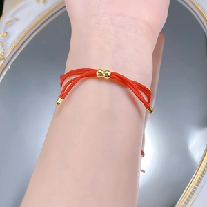 Detail of red braided string bracelet with gold beads over white floral mirror