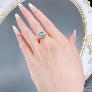 Detail of emerald cut blue topaz ring with diamond halo on golden band for women