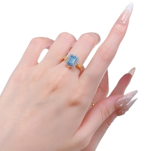 Elegant halo ring with rectangular sky blue stone and gold band on a hand