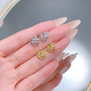 Detail of woven heart stud earrings in gold and silver held in hand with zircon accents