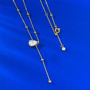 Detail of gold teardrop crystal necklace with bead accents on blue silk background