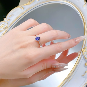 Detailed view of an oval blue sapphire ring on a finger with mirror reflection
