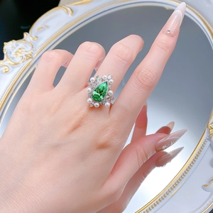 Macro detail of pear-cut emerald green gemstone and pearl inlay on a silver ring